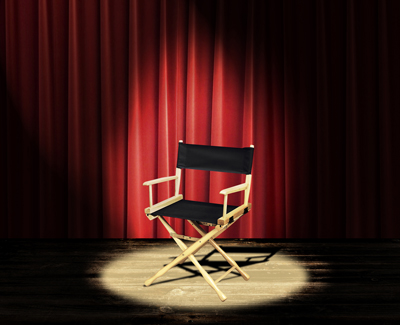 empty director's chair on stage with red curtains
